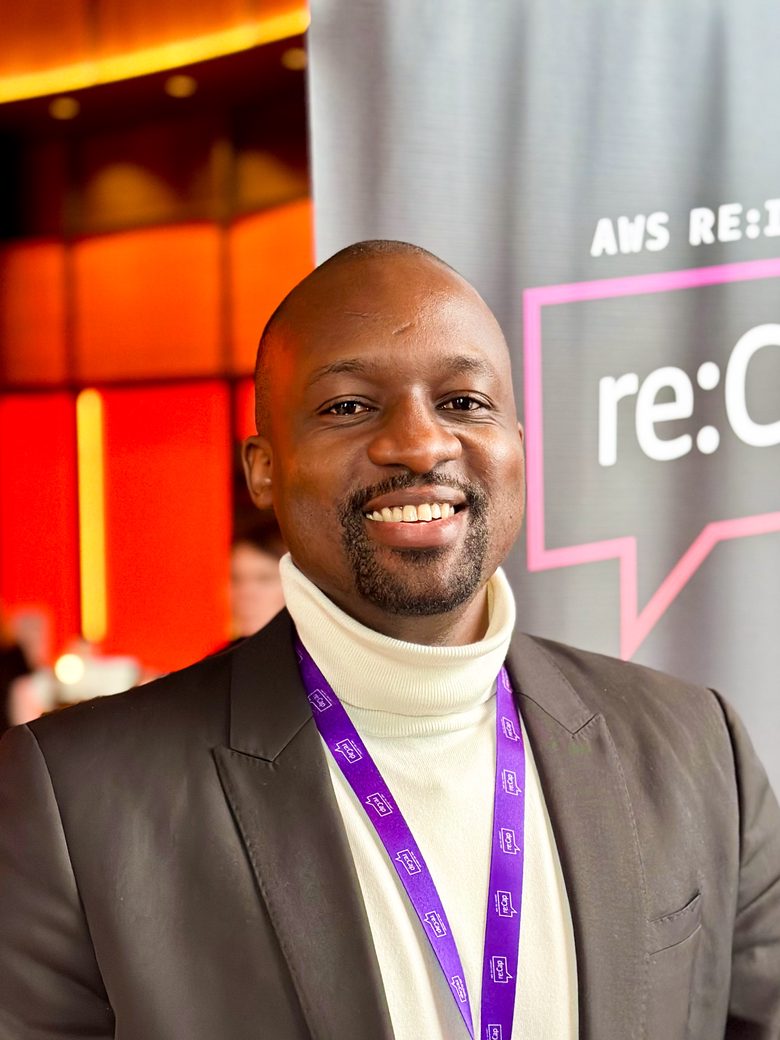 Tino Chemvura, smiling, in a dark blazer and cream turtleneck at AWS re:Invent